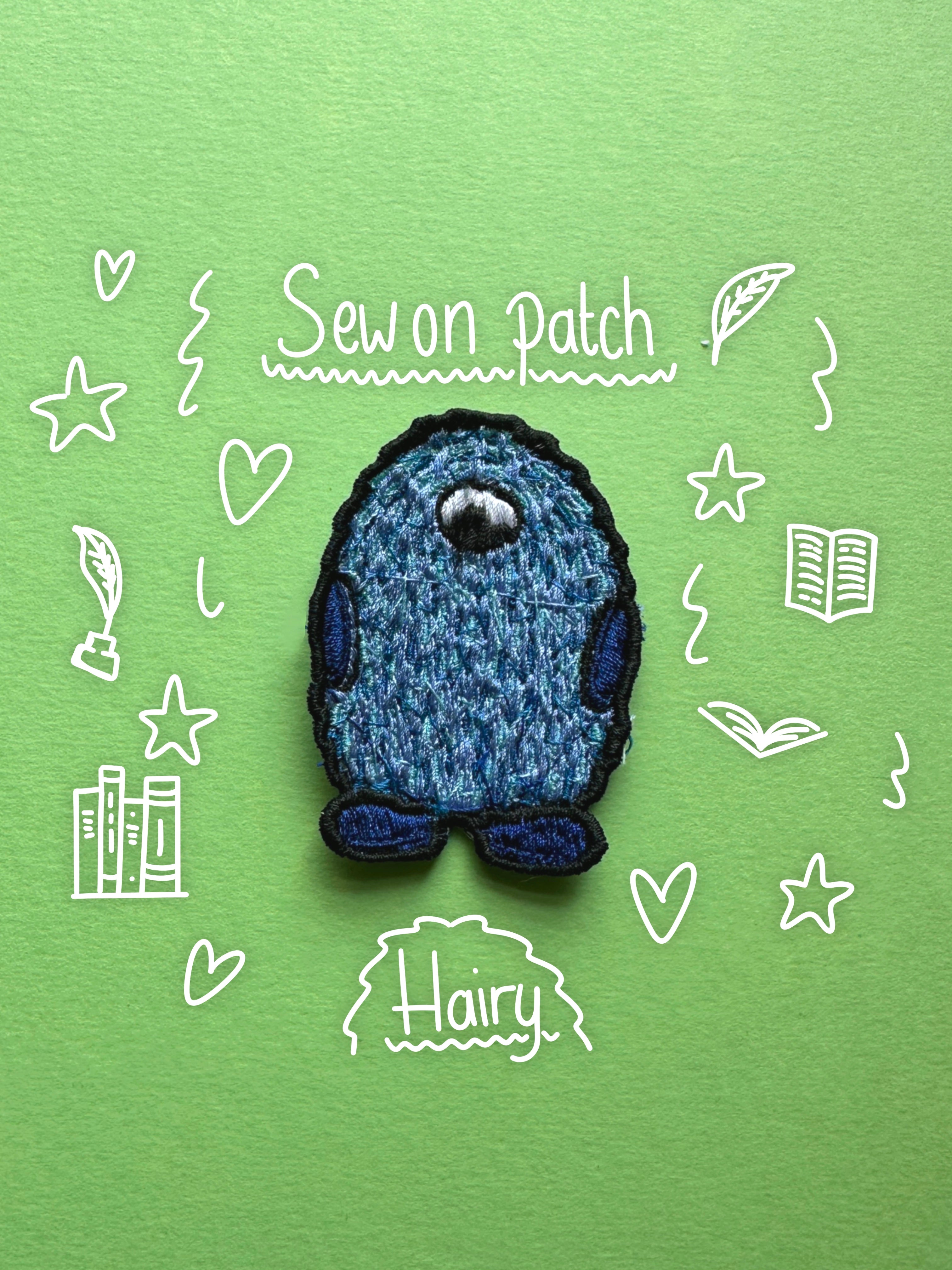 A small blue and navy embroidered monster patch with a single white eye, placed on a light green background with white hand-drawn doodles and the words 'Sew on Patch' and 'Hairy'.