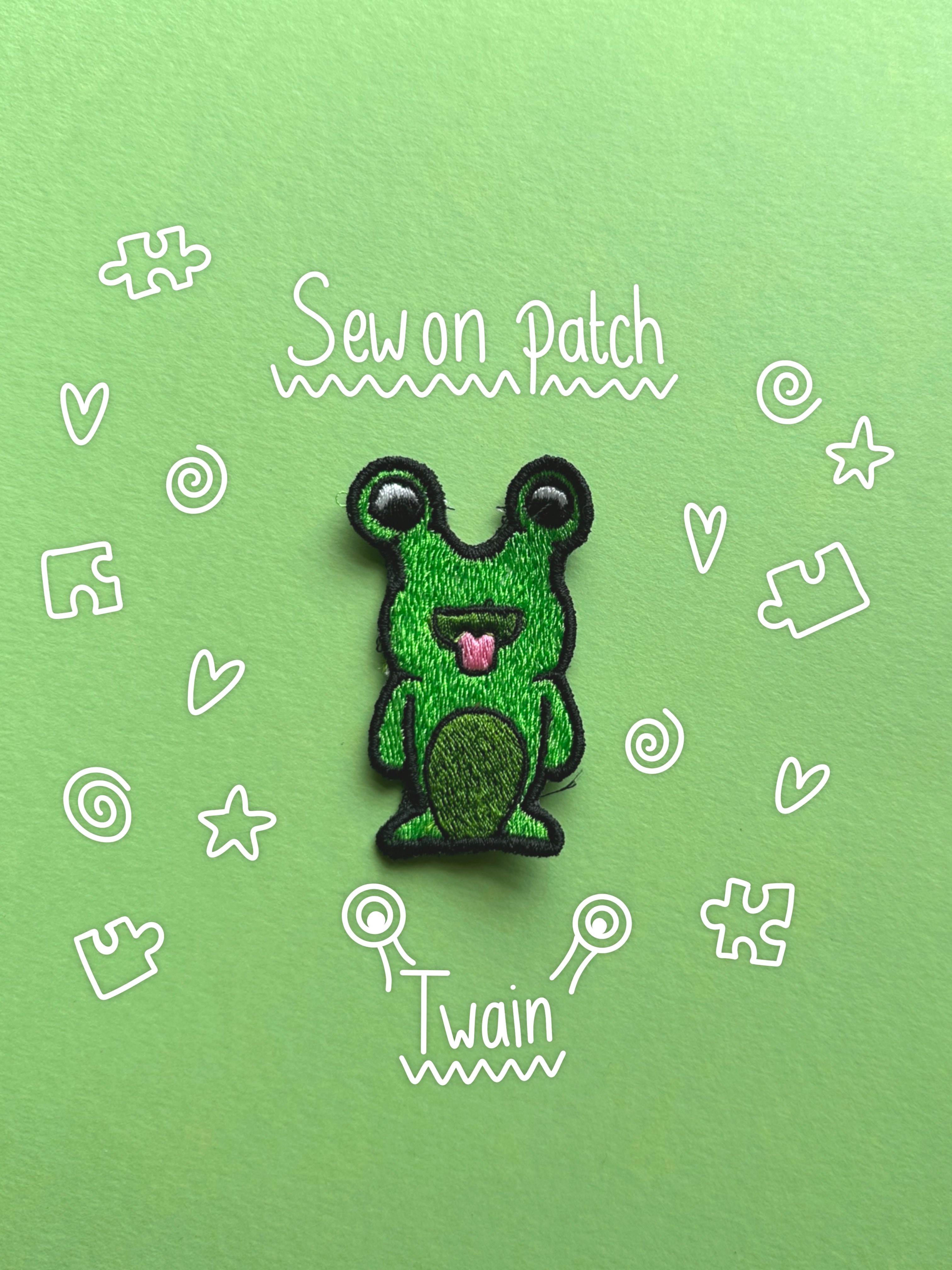 A green embroidered monster alien patch with black outlines and a pink tongue, centered on a light green background with white hand-drawn doodles and the words 'Sew on Patch' and 'Twain'.